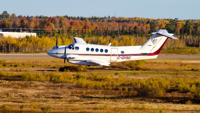 An aircraft taking off on a runway, with a backdrop of autumn-coloured trees.